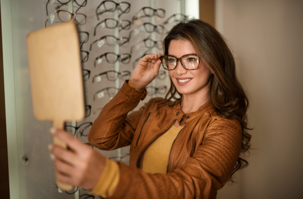 A woman trying on glasses and looking into a handheld mirror to see how she looks