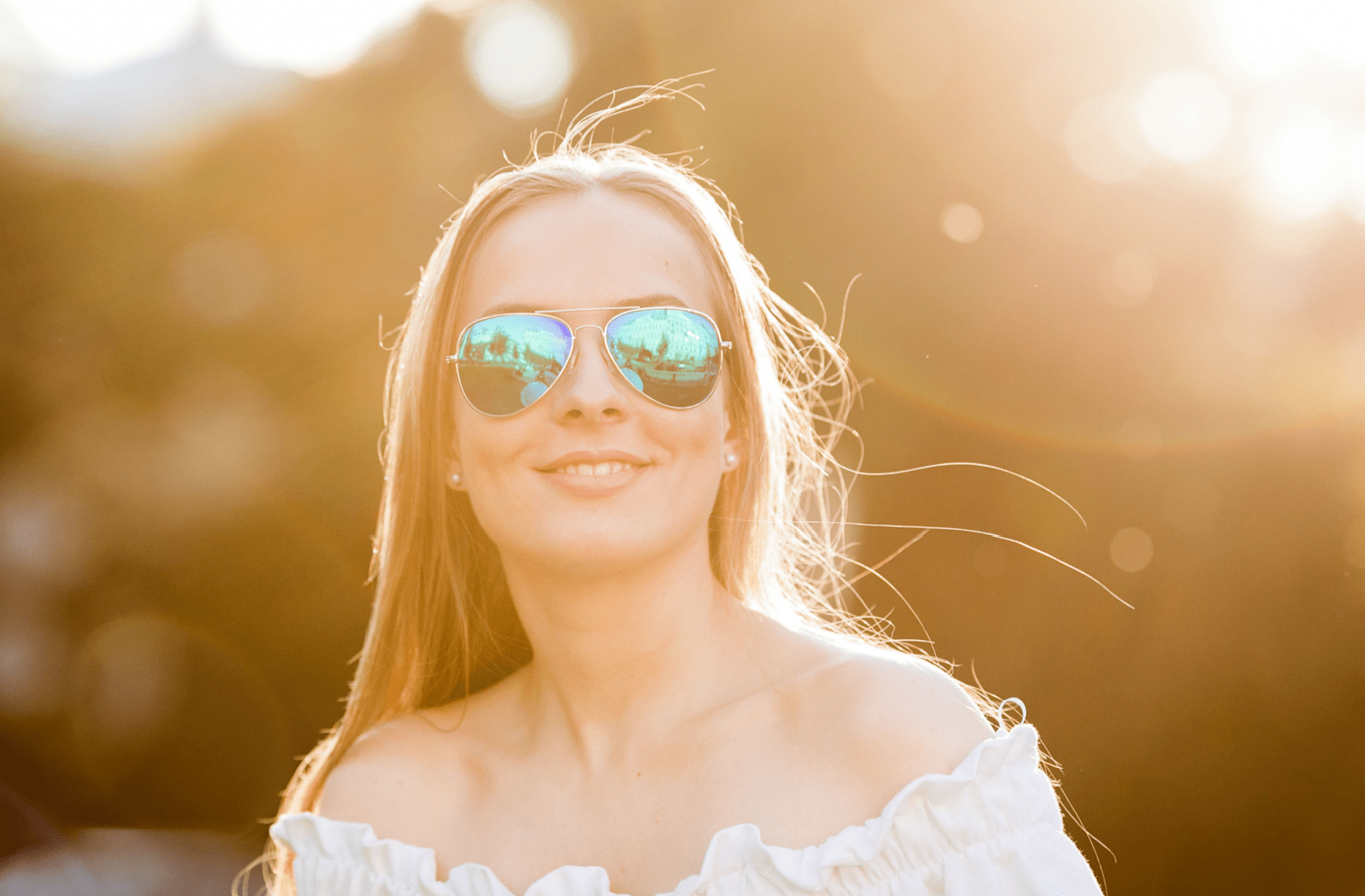 A young woman standing outside in the sunlight, wearing polarized sunglasses to protect her vision.