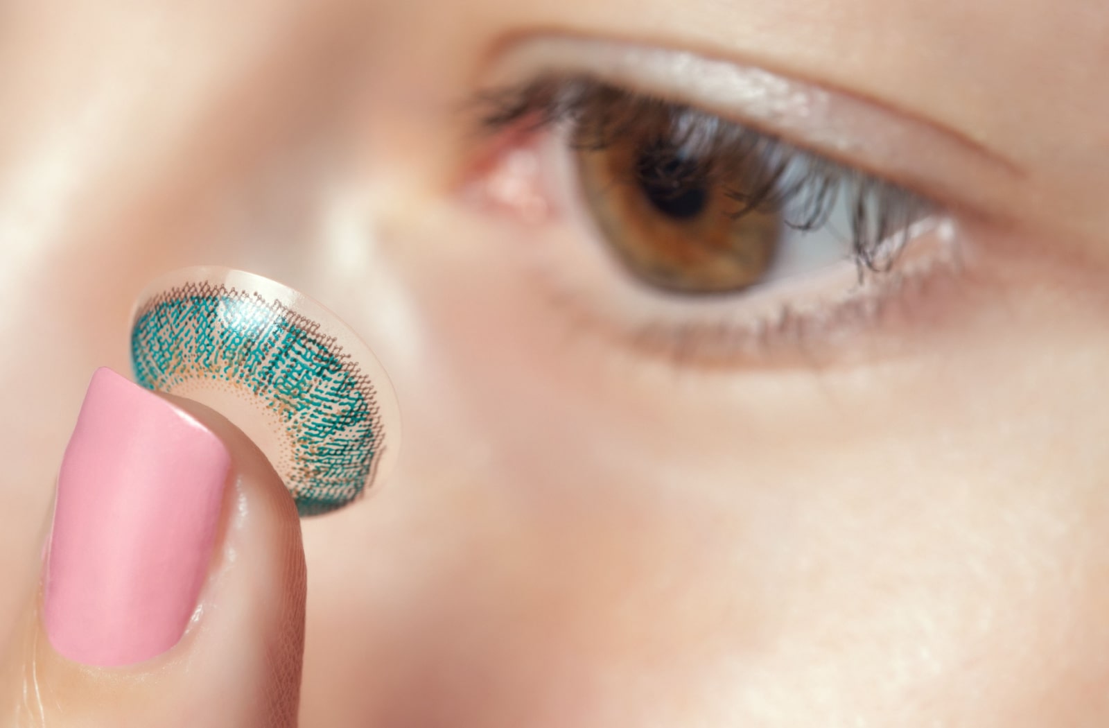 A woman holds a coloured contact lens on her index finger before placing it in her eye.