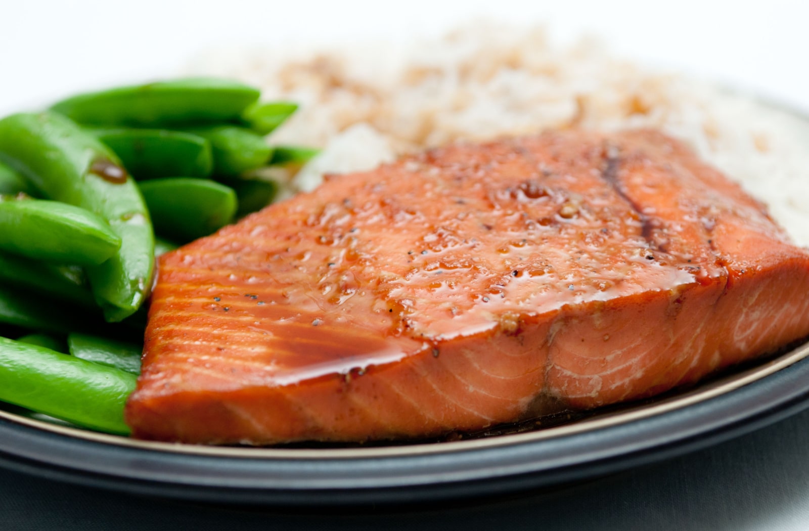 A maple glazed salmon on a plate with green beans and white rice