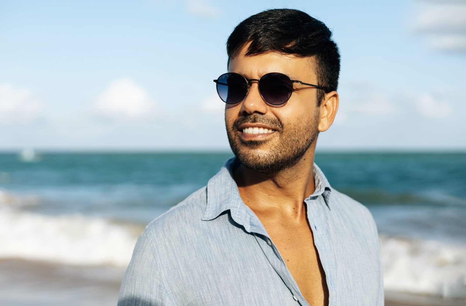 A man smiling and wearing polarized sunglasses at the beach.