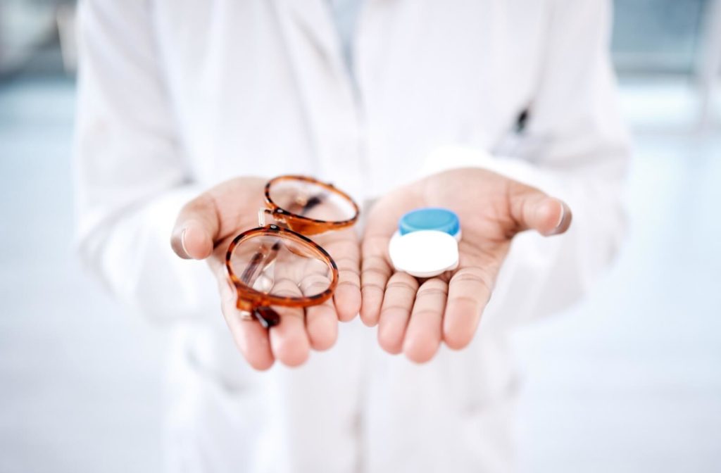 An eye care professional is holding glasses in one hand and contact lenses on the other hand.