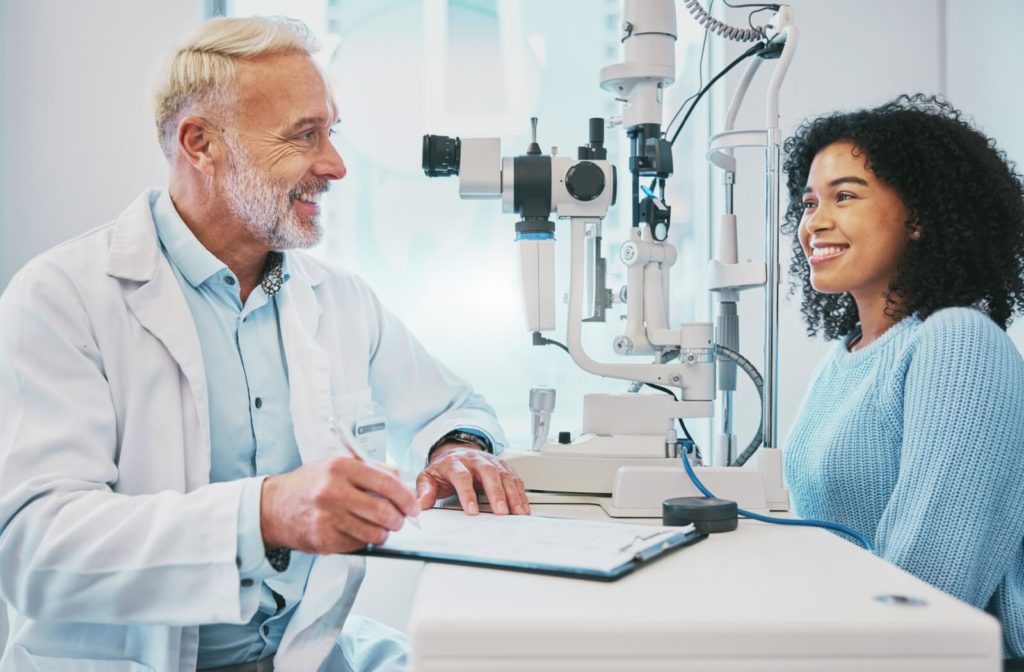 A mature optometrist and a young patient smiling at each other while discussing the results of an eye exam.