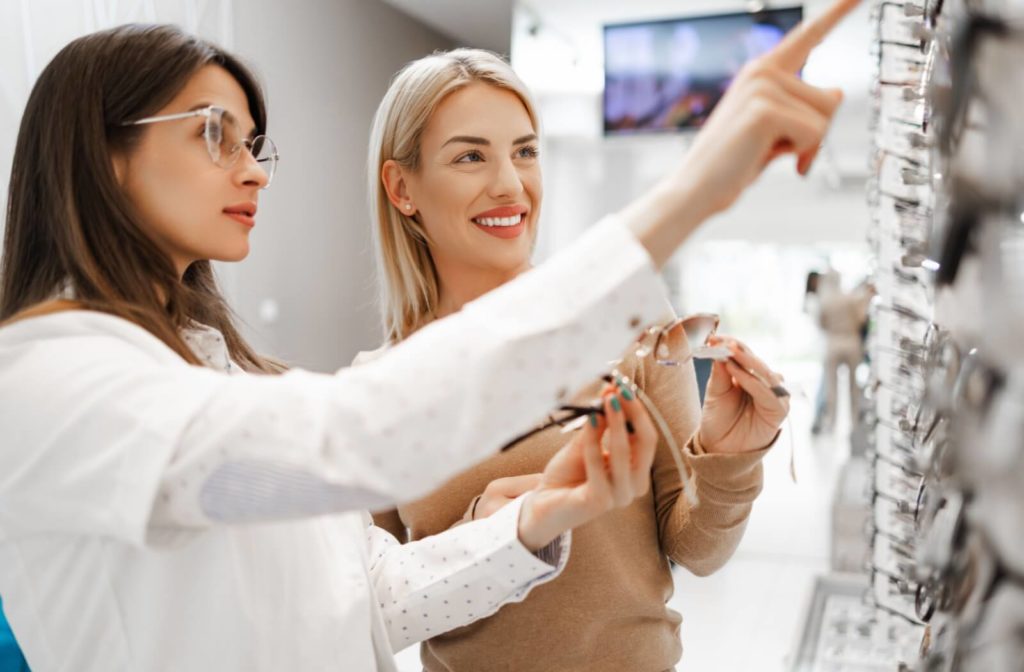 An optometrist helping her smiling patient choose between different sets of glasses in front of a display of frames.