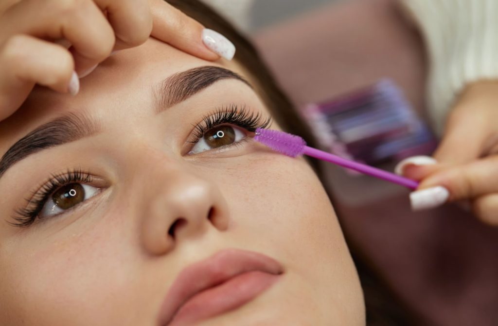 Eyelash technician combs the eyelashes of the client after the eyelash extension procedure.