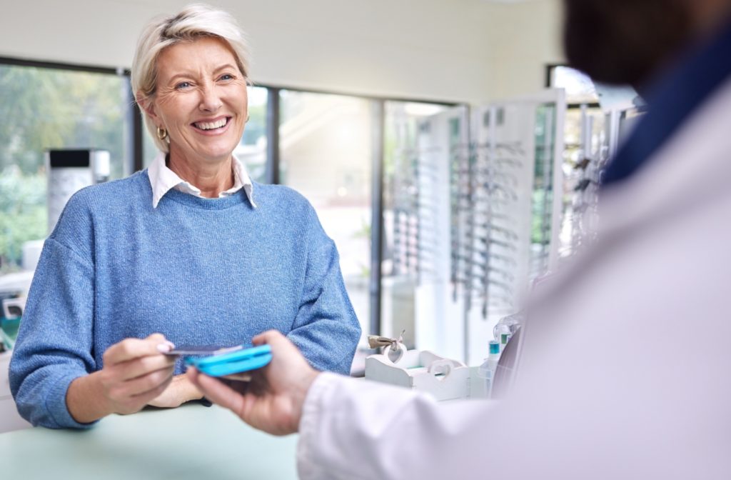 Older adult paying for an eye exam with a credit card in an optometry clinic.